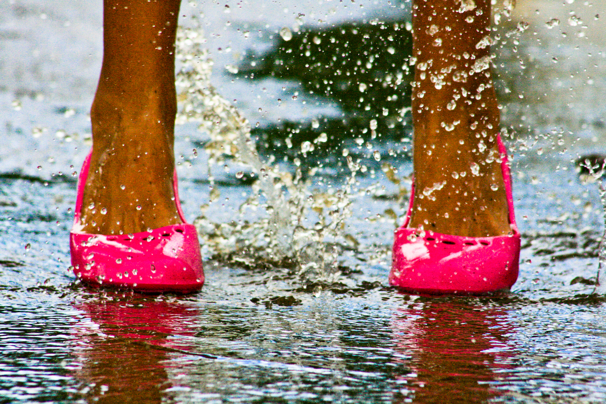 Clearly adult feet in bright fuchsia heels splashing through shallow water.
