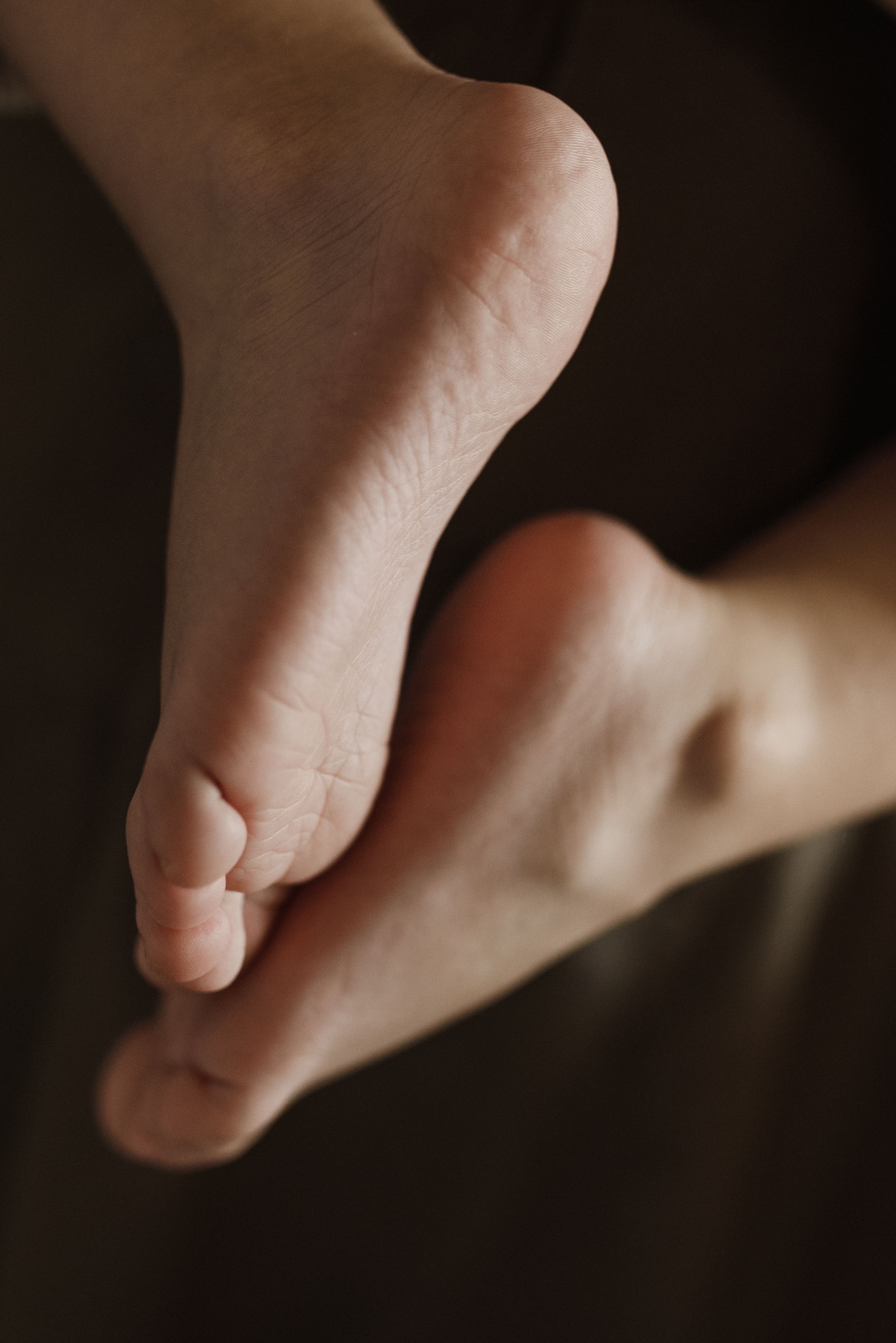 Adult bare soles in a warm, softly lit close-up against a dark background.