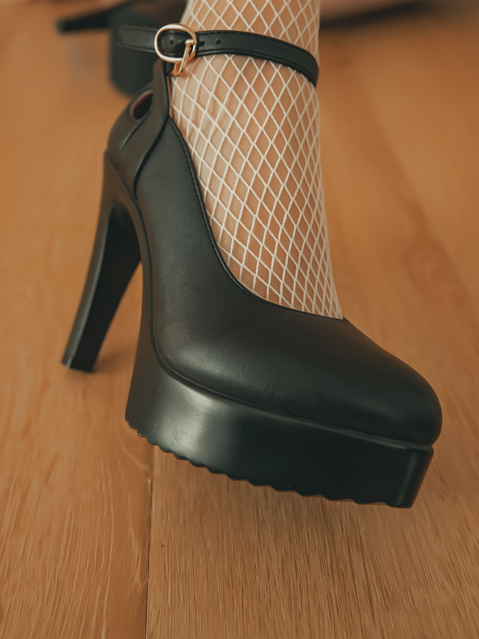 Clearly adult lower leg in fishnet stockings and a glossy black platform heel in a warm close-up.